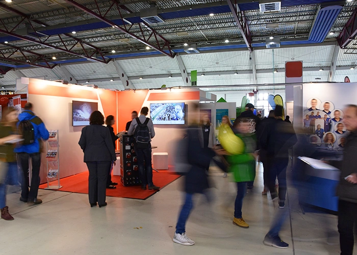 Visiteurs dans l'allée d'un hall d'exposition face aux stands de salon